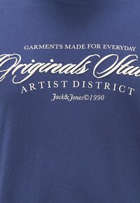 Navy blue cotton t-shirt featuring white printed text: "Garments made for everyday," "Originals Studio," and "Artist District."