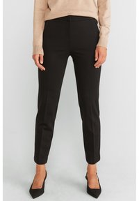 Mustat slim-fitti housut, joissa on räätälöity muotoilu, sileä pinta ja kapenevat lahkeet. Yhdistetty vaaleanbeigeen villapaitaan ja mustiin korkokenkiin.