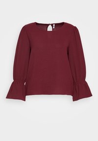 Burgundy paita pitkillä, puffimaisilla hihoilla ja röyhelöjoustimilla. Yksinkertainen tekstuuri ja avaus takana avaimenreijällä. Pyöreä kaula-aukko.