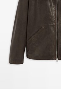 Dunkelbraune Lederjacke, Abschnitt mit linkem Ärmel, schräg eingesetzter Tasche und einem silbernen Reißverschluss vor weißem Hintergrund.