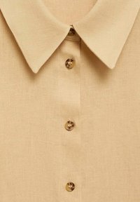 Camicia di lino beige con colletto a punta e sei bottoni rotondi. Tessuto morbido con un delicato motivo a trama.