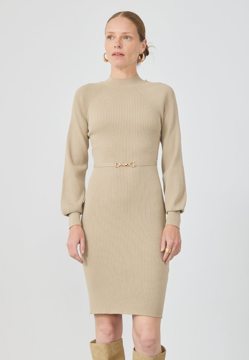 Beige ribbet strikkjole med lange ærmer, høj halsudskæring og guldtonet spænde detalje i taljen. Glat tekstur, tætsiddende design.