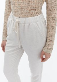 Lichtbeige, gestructureerde linnen broek met een elastische tailleband en aantrekkoord. Voorzien van zijzakken en een ontspannen pasvorm.