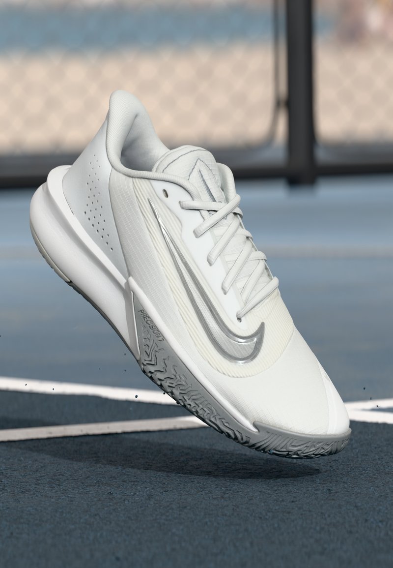 White athletic shoe with a textured upper, silver accent along the side, and a patterned rubber outsole; features lace-up design and padded collar.