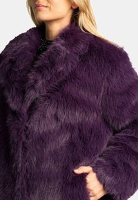 Abrigo de piel sintética púrpura con una textura suave, que presenta un amplio collar, bolsillos profundos y un ajuste relajado. Patrón de degradado distintivo en la piel.