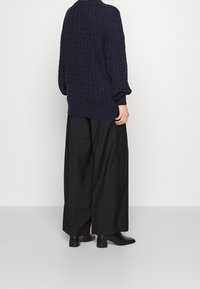 Pull en maille bleu marine avec motif texturé, coupe décontractée et manches larges, associé à un pantalon noir ample et des bottines à bout pointu.