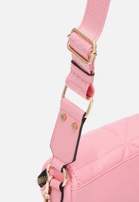 Pink quilted handbag with a textured finish, featuring a gold-tone adjustable strap and hardware, and black accent edges.