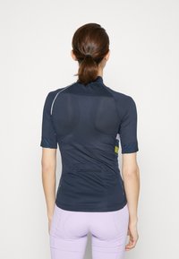 Top sportif à manches courtes bleu marine avec texture en maille, poche zippée à l'arrière et accents de couleur contrastants. Design lisse et ajusté.