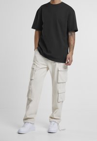 Černé oversized tričko z bavlny, kombinované se béžovými cargo kalhotami se čtyřmi bočními kapsami a bílými teniskami. Jednoduchý a funkční design.