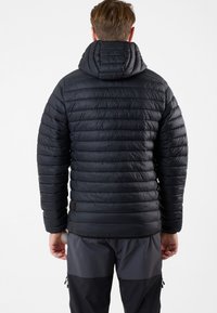 Zwarte gewatteerde jas met een horizontaal quiltpatroon, welke een vaste capuchon en elastische manchetten heeft. De jas heeft een strakke, gladde textuur en ritszakken.