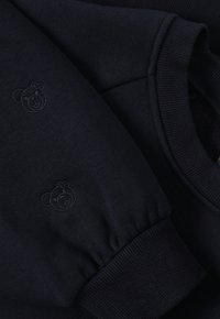 Sweat-shirt bleu marine avec une texture douce, des poignets côtelés et une broderie discrète d'ours sur la manche. Design simple et classique.