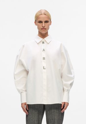 White cotton shirt featuring a classic collar, oversized sleeves, and a front placket with metallic letters spelling "KARL."