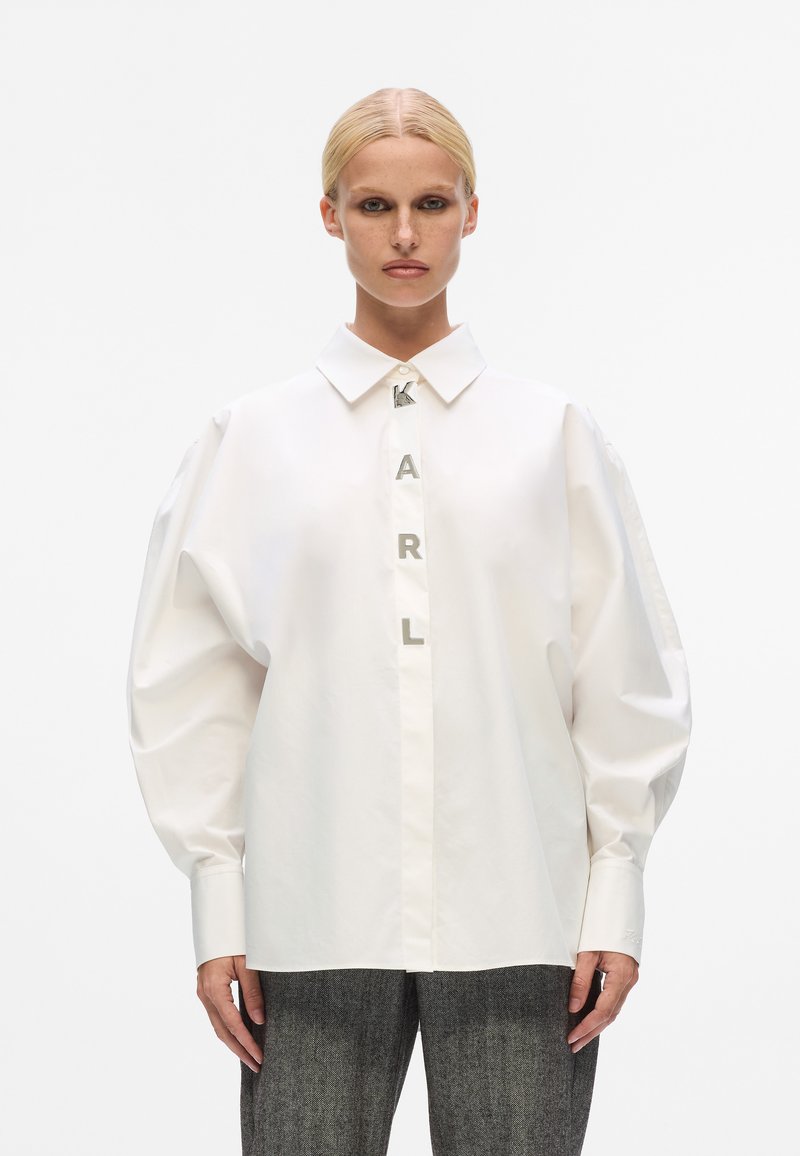 Witte katoenen shirt met een klassieke kraag, oversized mouwen en een voorkant met een knoopsluiting waarop metalen letters "KARL" staan.