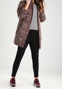 Brun puffjacka med hög krage, zipframslutning och elastisk midja. Matchad med en svart och vit randig topp och svarta slim-fit byxor.