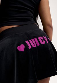 Μαύρη φούστα από βελούδο με φαρδιά γραμμή, διαθέτει έντονα ροζ γράμματα "JUICY" και μια καρδιά κοντά στη μέση, με απαλή υφή.