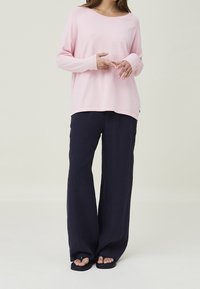 Rosa långärmad topp med rund halsringning, kombinerad med marinblå vida byxor. Tyget verkar mjukt, med en avslappnad passform och avslappnad stil.