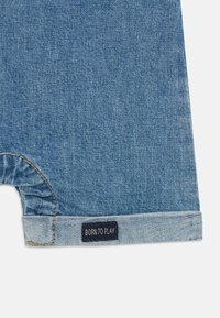 Denim kratke hlače svetlo modre barve, z raztrganim robom, zloženim manšetom in črno etiketo z napisanimi besedami "RODJEN ZA IGRO".