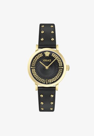 Reloj dorado con correa de cuero negra, que presenta tachuelas doradas, un dial negro con patrón y un diseño de clave griega. Logo de Versace en la parte superior.