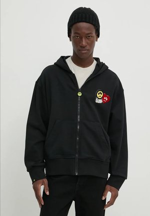 Felpa nera con zip in tessuto morbido, dotata di tasche frontali, con ricami colorati di faccine sorridenti e cuori sul lato sinistro del petto.