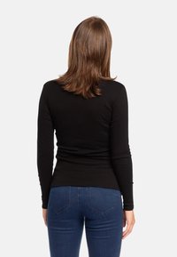 Maglietta nera a maniche lunghe realizzata in tessuto elasticizzato, design aderente con cuciture laterali, indossata con jeans blu, che mostra una silhouette semplice e pulita.