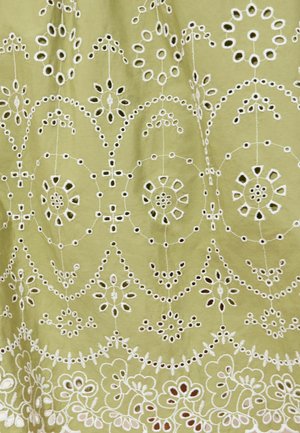 Jasnozielona tkanina z misternymi, białymi, haftowanymi wzorami kwiatowymi i okrągłymi, zawierającymi symetryczne wycięcia.
