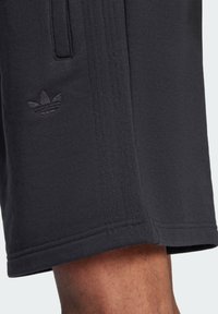Schwarze Sportshorts mit strukturiertem Finish, ausgestattet mit Seitentaschen, vertikalen Nahtdetails und einem gestickten Logo am Saum.