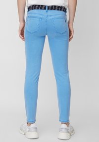 Los vaqueros ajustados de color azul claro tienen una textura suave, cinco bolsillos y una cinturilla a rayas en blanco y negro. Combinados con zapatillas blancas.