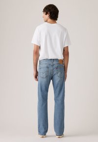 Ανοιχτό μπλε τζιν με ίσια γραμμή, με πίσω τσέπες και καφέ δερμάτινο λογότυπο. Φοριέται με λευκό μπλουζάκι.