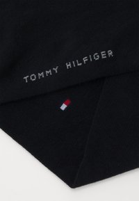 Fekete kötött sál, rajta szürke színnel "TOMMY HILFIGER" felirattal. Az éle körül egy kis piros, fehér és kék csíkos logó található. Puha tapintású.
