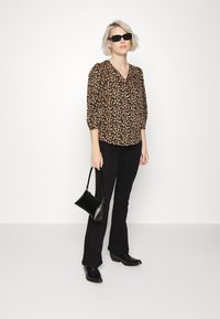 Blusa de estampado leopardo castanho com mangas bufantes, combinada com calças pretas flare e botas pretas de salto. Uma pequena bolsa preta realça o conjunto.