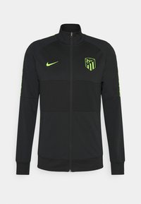 Chaqueta negra con cremallera fabricada en tejido suave, con un alto collar, logo verde de Nike y emblema del club en el pecho; puños acanalados.
