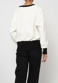 Pull blanc texturé avec un ourlet côtelé noir et un col noir. Présente des manches longues et une coupe décontractée, vu de dos.