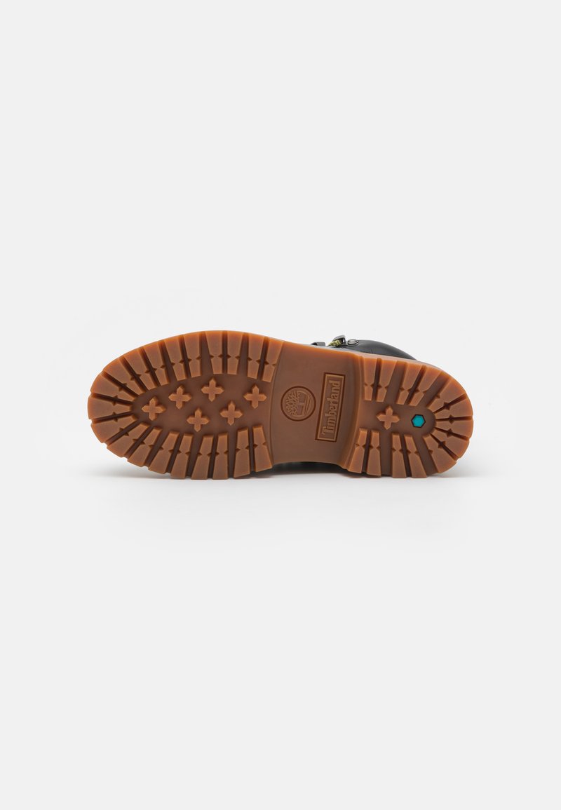 Stivale nero con suola in gomma marrone robusta caratterizzata da scanalature profonde, logo in rilievo e un accento colorato vicino al tallone.