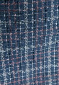 Modrý vzorovaný textil s mřížkovým designem. Obsahuje růžové a bílé nitě, které vytvářejí texturovaný, tkaný vzhled.