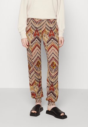 Pantalons à motifs dans des tons chauds, présentant des designs en zigzag et géométriques, avec des chevilles froncées, fabriqués en tissu léger.