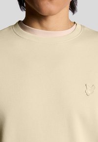 Felpa a girocollo color beige chiaro realizzata in tessuto texturizzato, con un ricamo del logo sottile sul petto e un design del colletto a strati.
