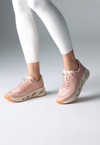 Baskets de sport rose clair avec un tissu texturé, bout arrondi et semelle épaisse beige avec des découpes. Lacets de couleur rose assortie.