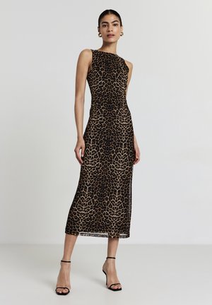 Frau, die in einem ärmellosen, figurbetonten Midikleid mit braunem und schwarzem Leopardenmuster steht, trägt schwarze High-Heel-Sandalen und goldene Creolen.