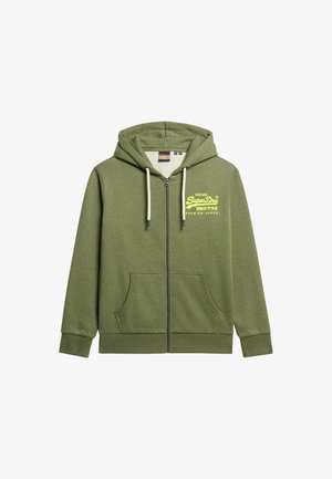 Sudadera verde con cremallera en un material suave, que presenta un logo frontal en amarillo, dos bolsillos laterales y una capucha con cordón.