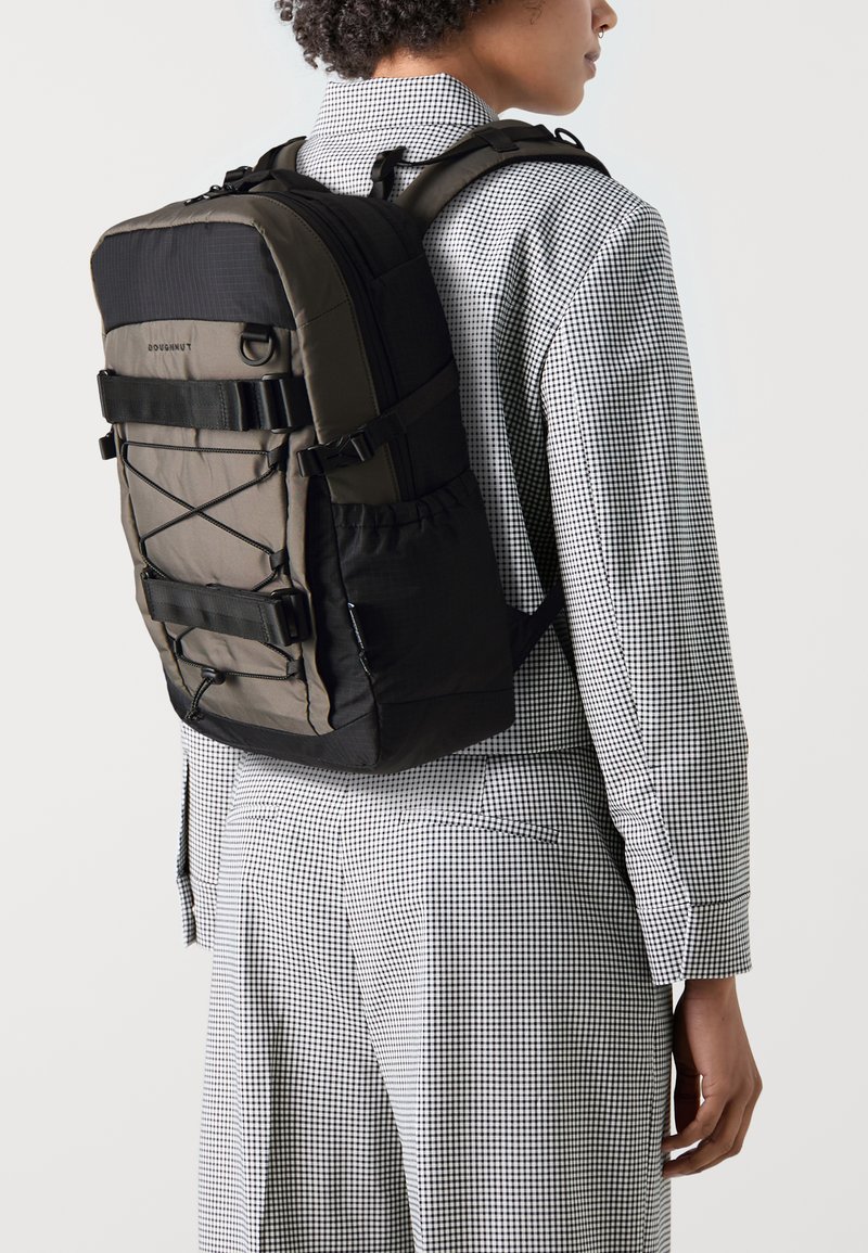 Sac à dos noir et gris avec un design structuré, des bretelles réglables, un détail de cordon élastique et un tissu texturé durable.