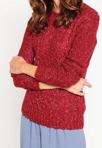 Red knitted sweater with a textured pattern, round neckline, and long sleeves. The fabric appears thick and warm, ideal for colder weather.