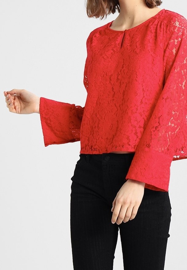 Red lace top with a round neckline, long bell sleeves, and a keyhole detail at the front, paired with black fitted pants.