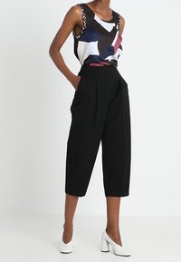 Färgglad ärmlös topp med abstrakta mönster, kombinerad med högmidjade svarta capribyxor och vita klackskor med blockhäl.