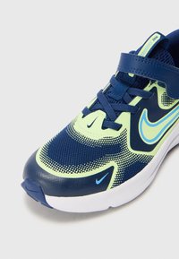 Baskets de sport bleu marine et vert fluo avec tige en mesh, accents en cuir texturé et swoosh bleu contrastant. Sangle ajustable sur les lacets.