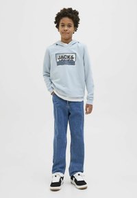 Svijetloplava dukserica s natpisom "JACK & JONES", u kombinaciji s plavim trapericama i crnim tenisicama. Dukserica ima prednji džep i kapuljaču sa vezicom.