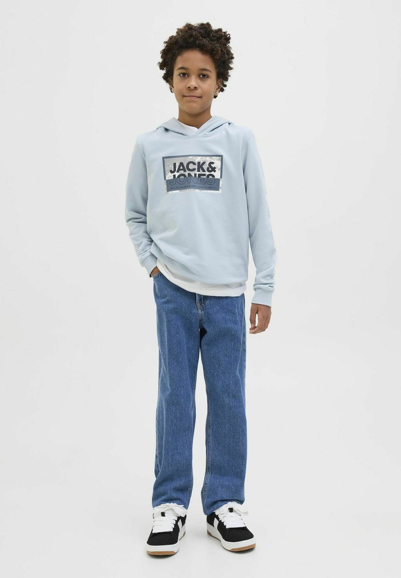 Svijetloplava dukserica s natpisom "JACK & JONES", u kombinaciji s plavim trapericama i crnim tenisicama. Dukserica ima prednji džep i kapuljaču sa vezicom.