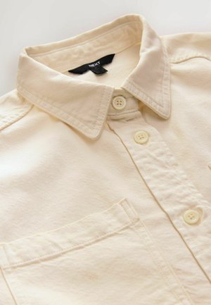 Camisa de botones color crema hecha de algodón texturizado, con cuello extendido, bolsillo frontal y botones de plástico.