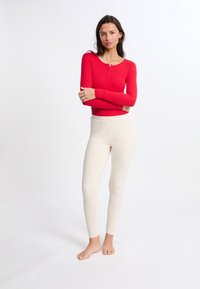 Cuerpo rojo de manga larga con botones en el escote, combinado con leggings ajustados de color crema. Ambos hechos de una tela suave y elástica.