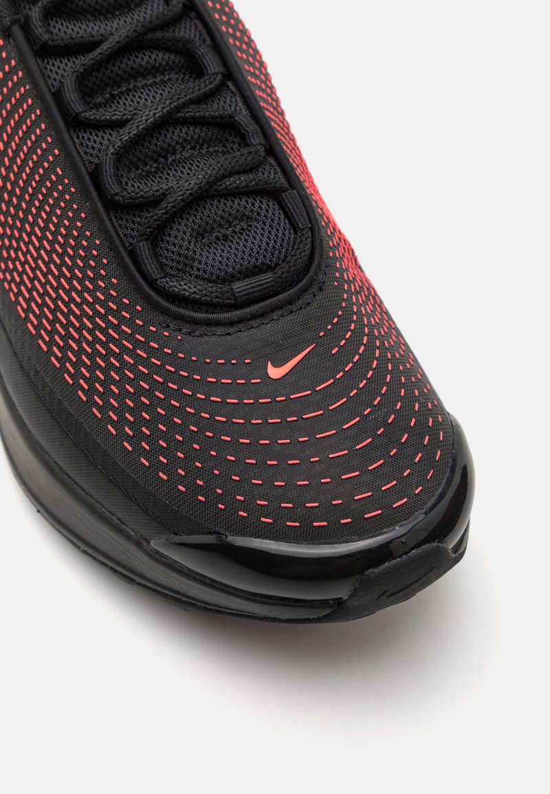 Chaussure de sport noire avec des motifs de points rouges, empeigne en maille, lacets et semelle noire brillante. Logo Nike rouge dans la zone des orteils.