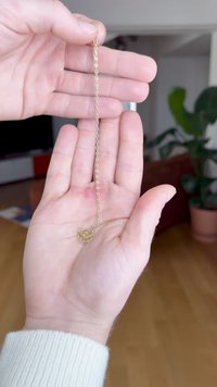 Aranyszínű fémlánc egy kézben tartva. A lánc kis ovális szemekből áll, és a végén összegabalyodott rész található.